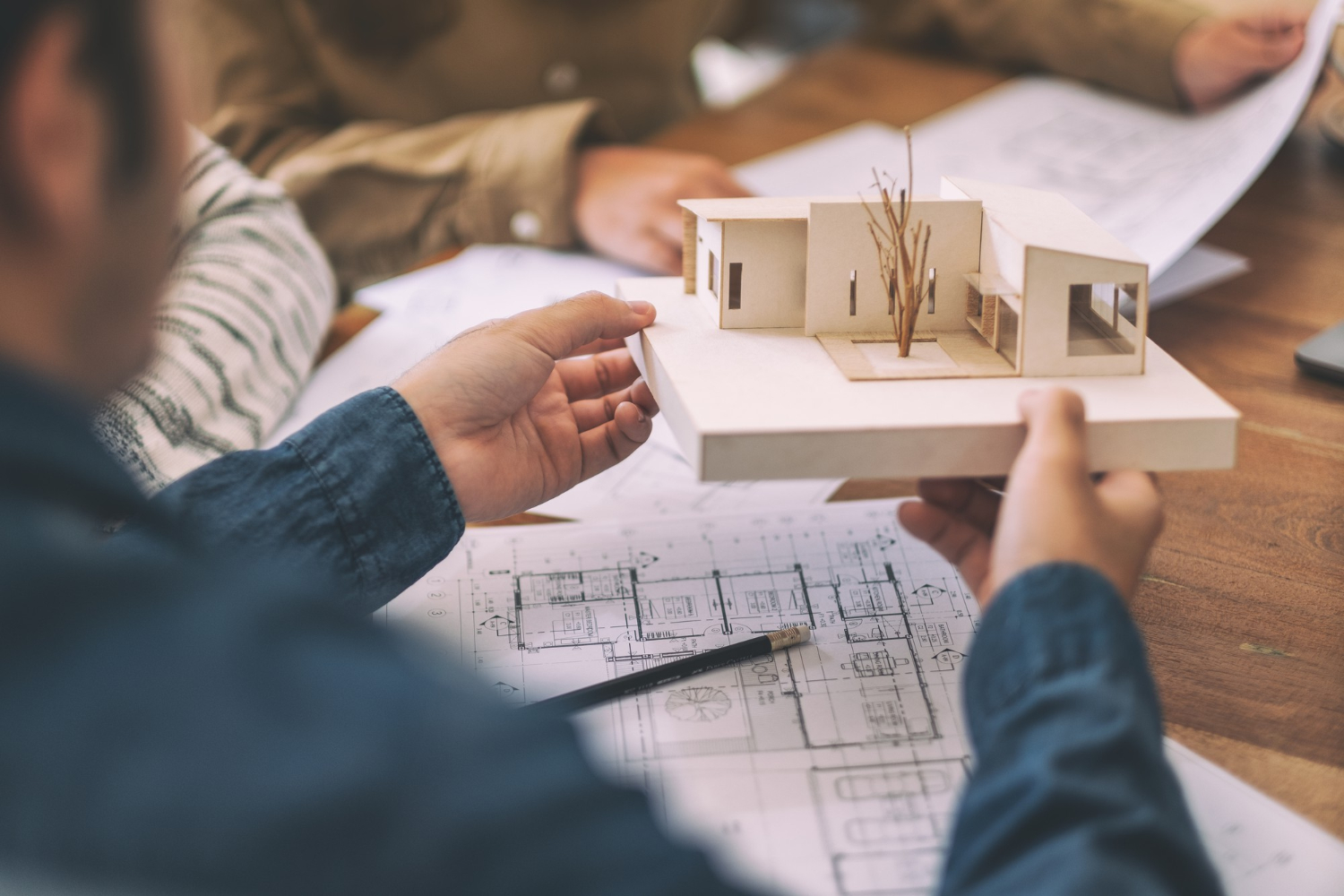 Groupe d'un architecte travaillant et discutant d'un modèle d'architecture avec du papier à dessin d'atelier sur une table au bureau